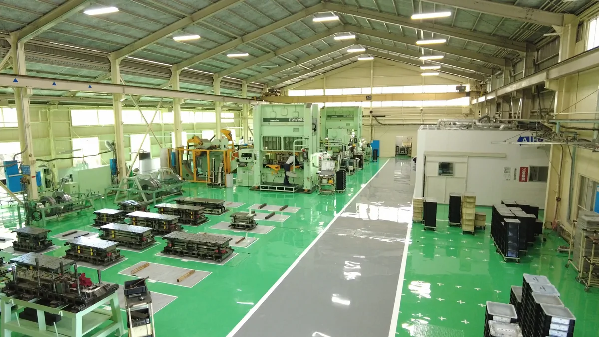 緑の床に金型が整然と並び、奥にプレス機が稼働する扶桑工場の製造現場